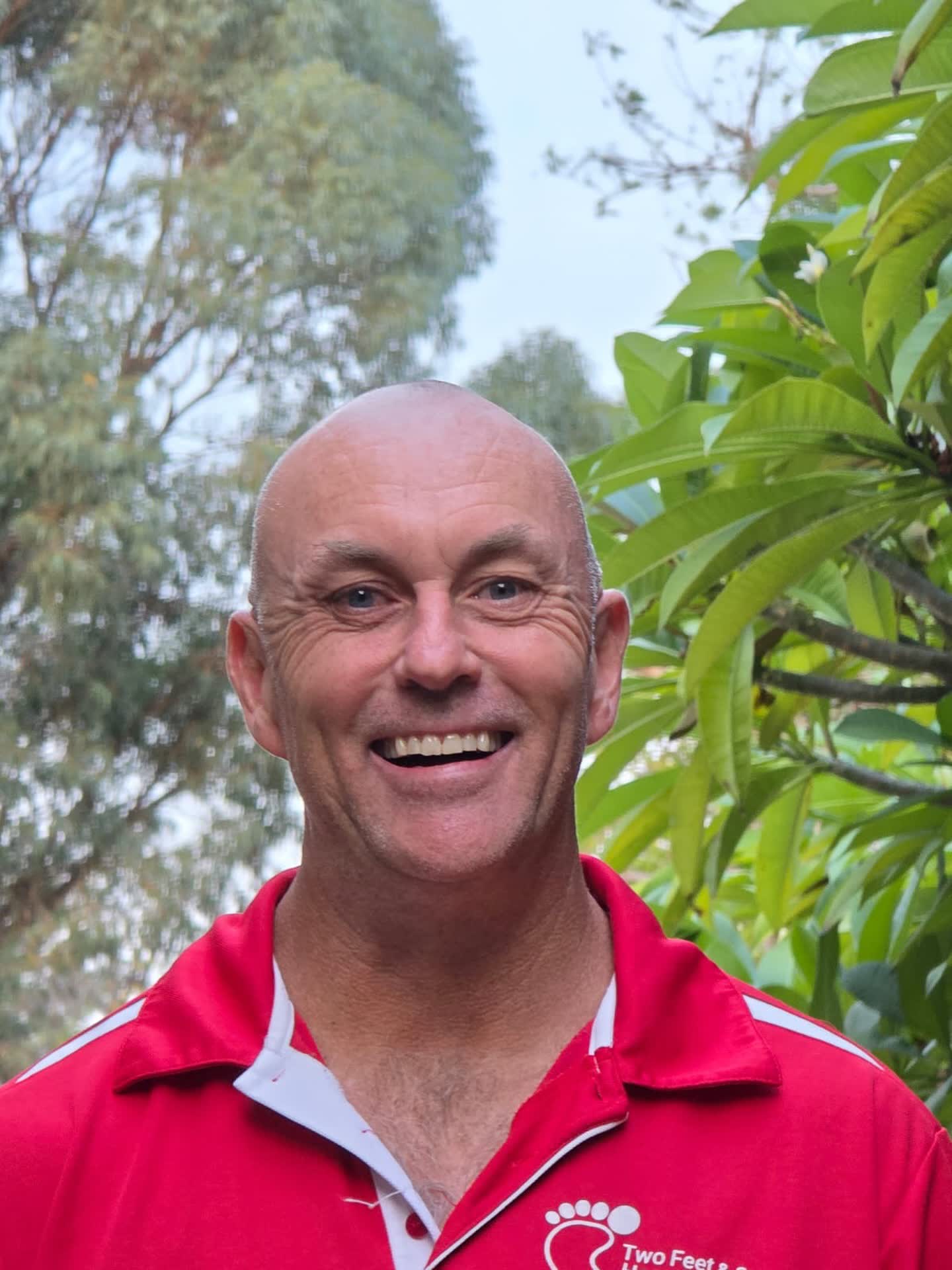 Two Feet guide Daniel smiling in his red Two Feet & a Heartbeat polo among garden greenery