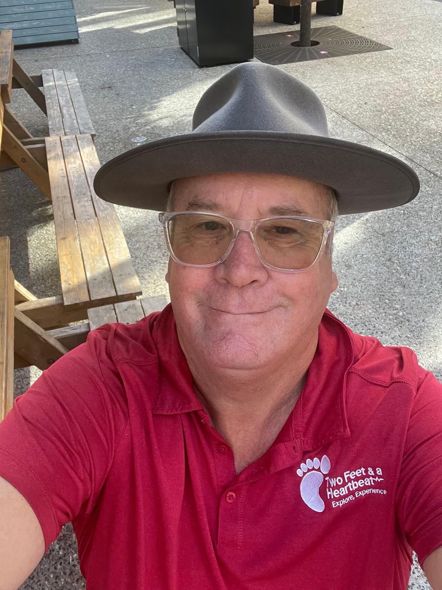 Two Feet guide Gerard in a wide-brim hat and glasses, wearing the red team polo at an outdoor table