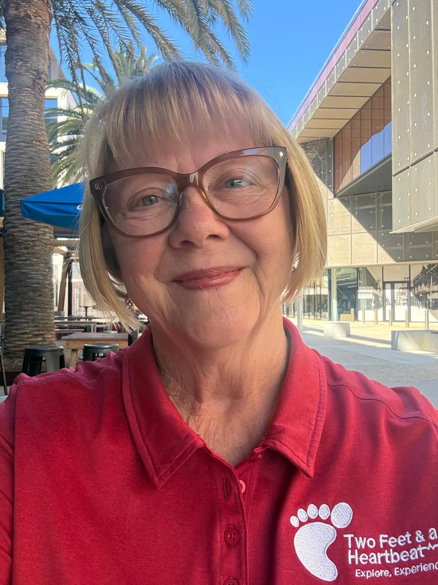 Two Feet guide Jen in glasses and the red team polo, smiling in a sunny city square with palm trees