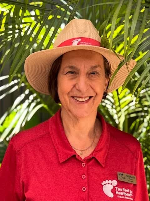 Two Feet guide Michelle in a straw hat with a Two Feet band, smiling among palm fronds