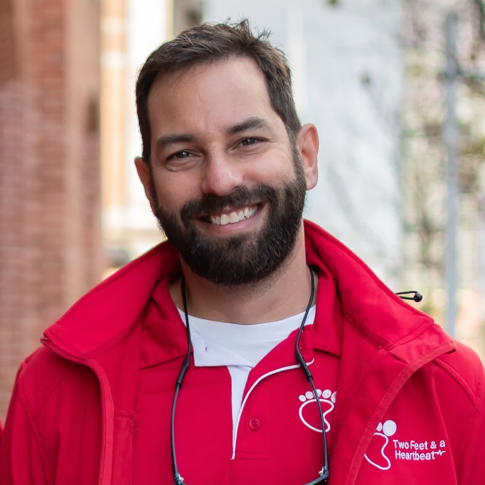 Two Feet co-founder Ryan smiling in a red team jacket on a heritage brick street