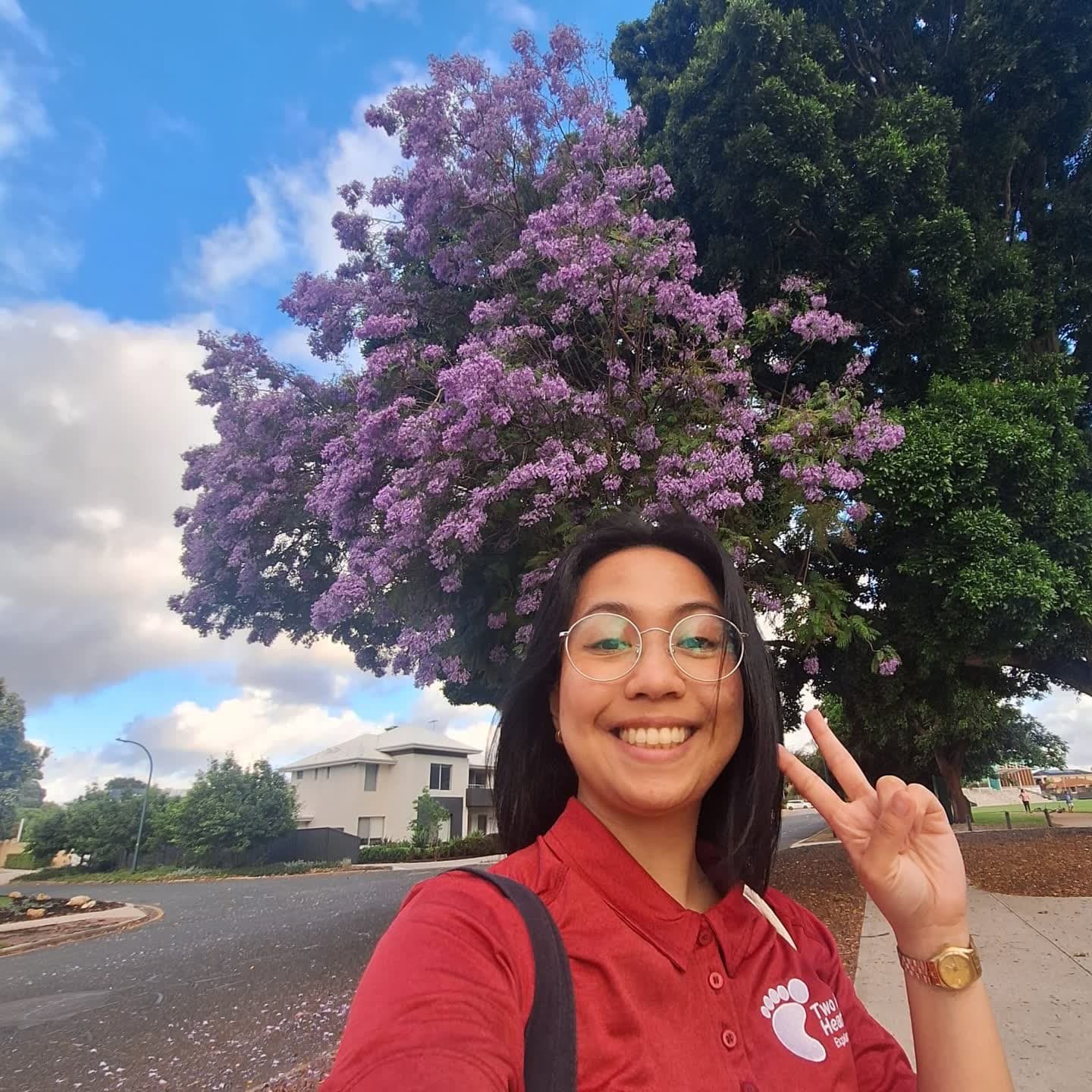 Two Feet guide Sam in round glasses giving a peace sign under a blooming jacaranda tree